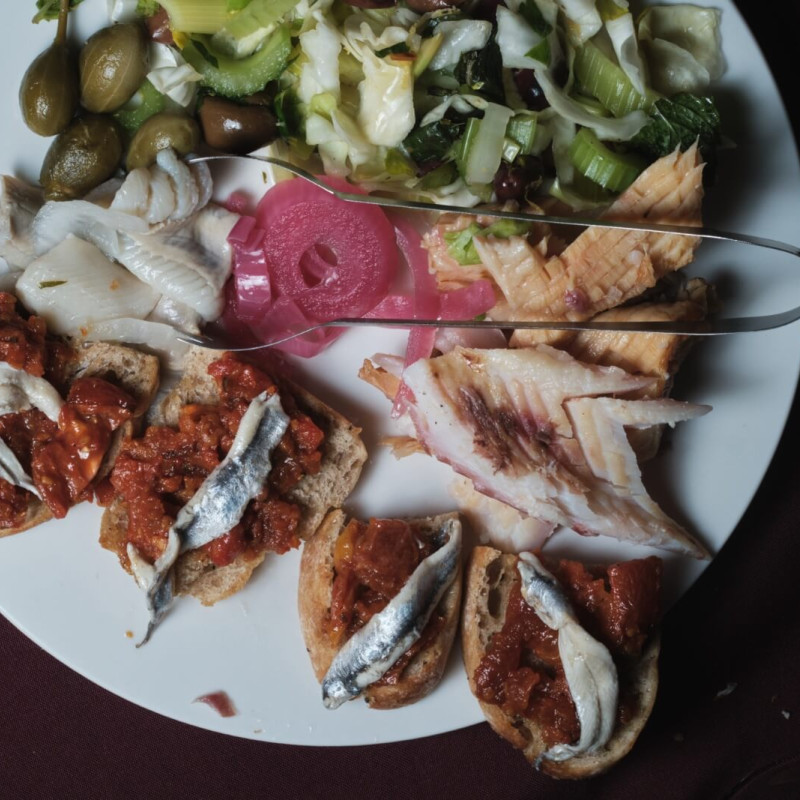 A plate of antipasti featuring fish, pickled vegetables, and olives