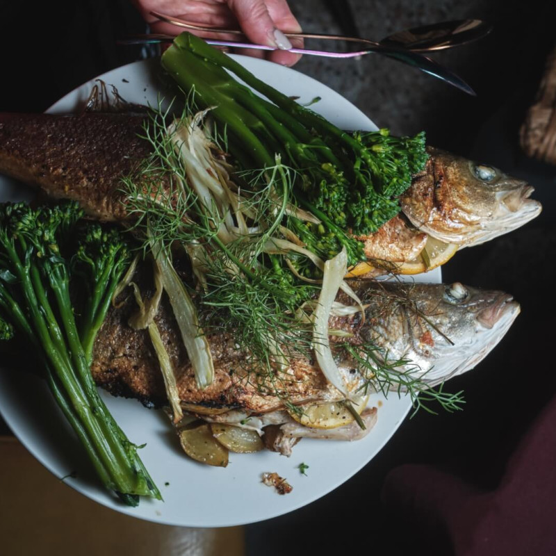 Two whole cooked fish on a plate, topped with green vegetables